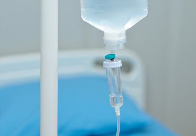 Капельница с прозрачной жидкостью висит на белой стойке в больничной палате